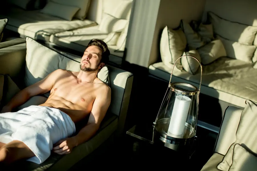 A guest resting with closed eyes on a lounger in a dim relaxation room